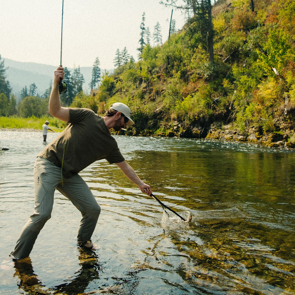 Man landing a fish wearing the Olive colored Standard Issue Tee 